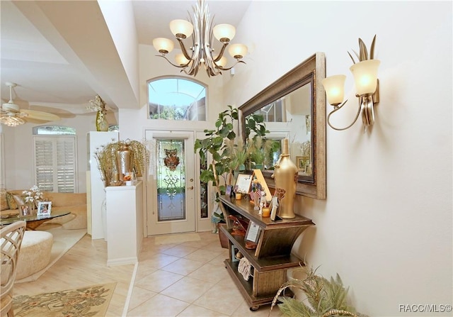 doorway to outside featuring a towering ceiling, light tile patterned floors, and ceiling fan with notable chandelier