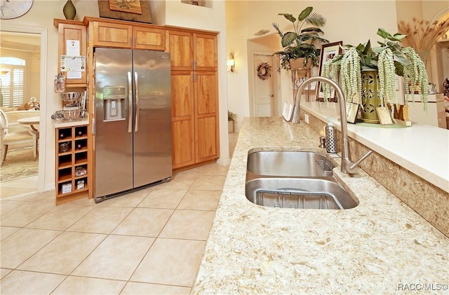 kitchen featuring stainless steel refrigerator with ice dispenser, light tile patterned floors, light stone counters, and sink