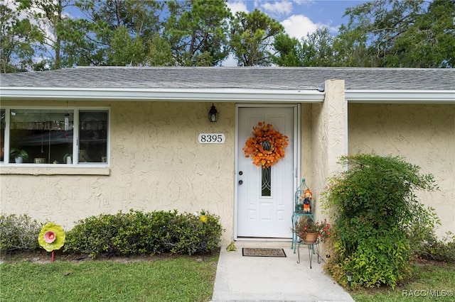 view of exterior entry with roof with shingles and stucco siding