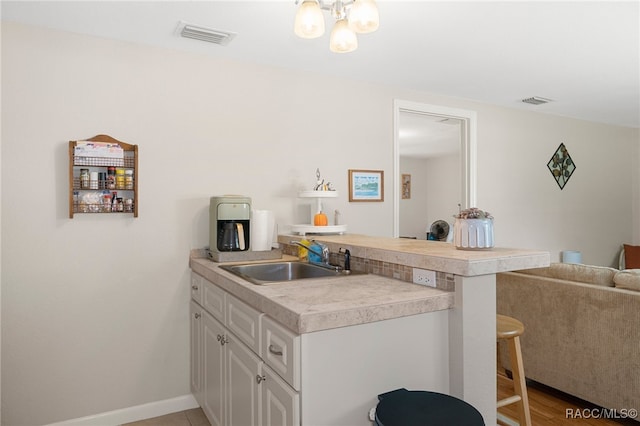 kitchen with a breakfast bar, light countertops, visible vents, white cabinets, and a sink