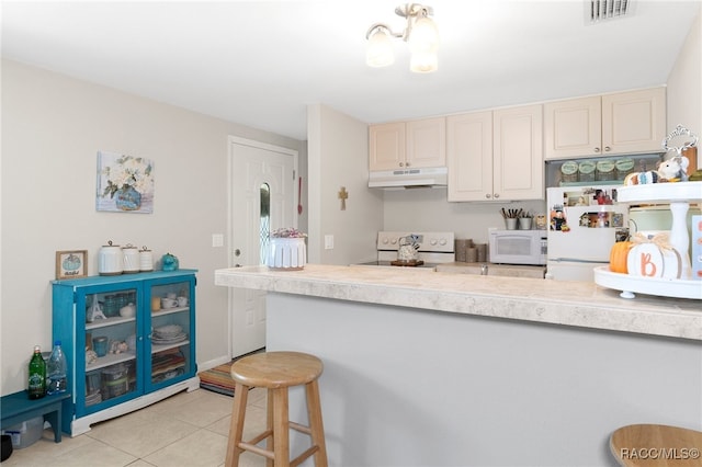 kitchen with a breakfast bar, light tile patterned floors, visible vents, white appliances, and under cabinet range hood