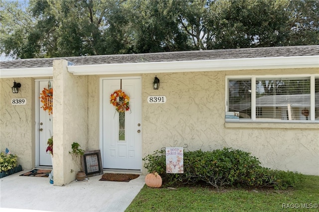 entrance to property featuring a shingled roof and stucco siding