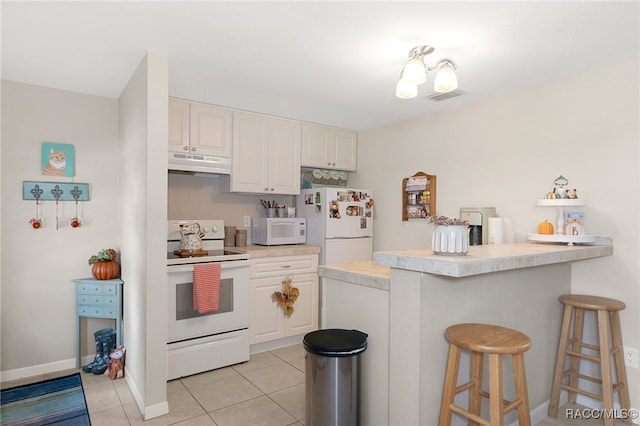 kitchen featuring light countertops, white cabinets, white appliances, under cabinet range hood, and a kitchen breakfast bar