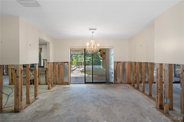 unfurnished dining area with concrete flooring, a textured ceiling, and an inviting chandelier