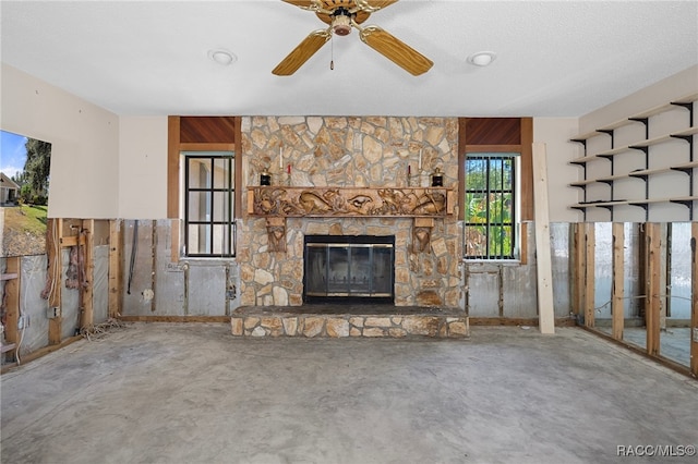 unfurnished living room with concrete floors, a stone fireplace, ceiling fan, and wood walls