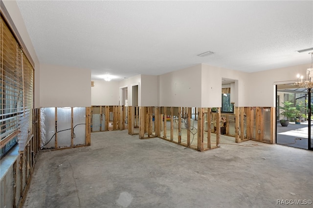 spare room with a notable chandelier, a textured ceiling, and concrete floors