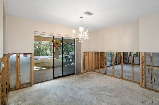 spare room featuring a notable chandelier, a textured ceiling, and concrete floors