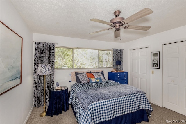 carpeted bedroom with ceiling fan, a textured ceiling, and multiple closets