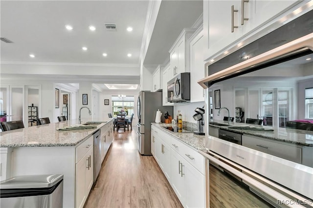 kitchen with a breakfast bar, a kitchen island with sink, sink, appliances with stainless steel finishes, and white cabinetry