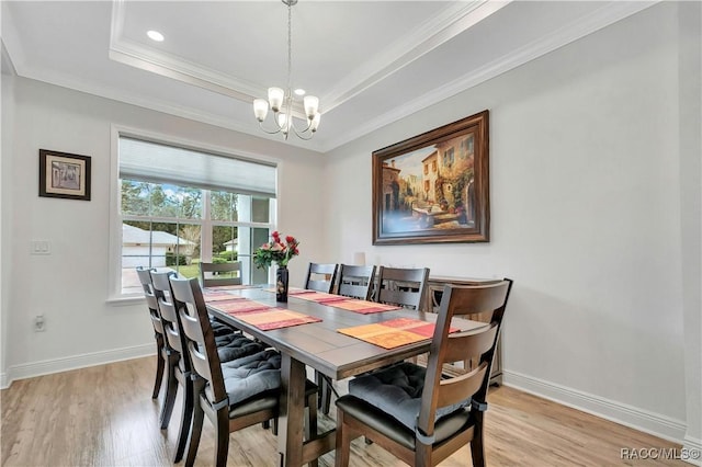 dining area with a notable chandelier, light wood-type flooring, ornamental molding, and a tray ceiling