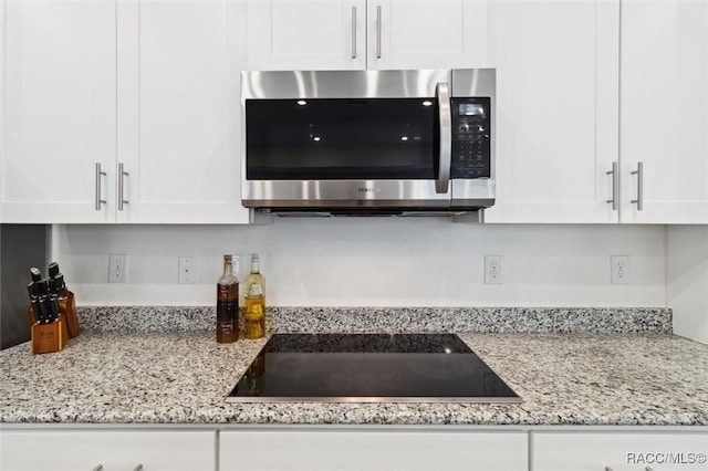 room details featuring light stone countertops, black electric stovetop, and white cabinetry