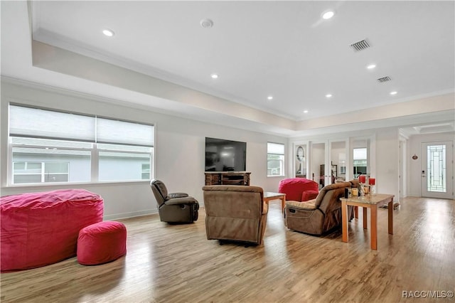 living room featuring light wood-type flooring, a raised ceiling, and crown molding