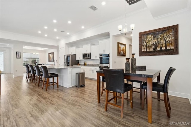 dining room with hardwood / wood-style flooring, sink, crown molding, and an inviting chandelier