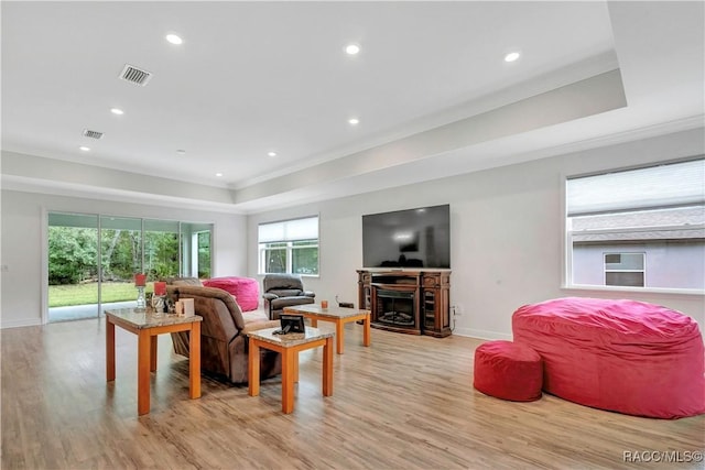 living room with light hardwood / wood-style floors, crown molding, and a tray ceiling