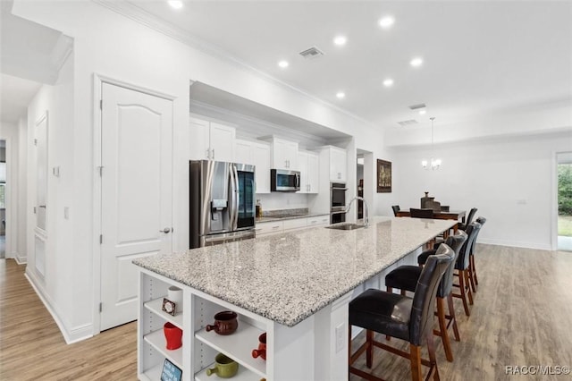 kitchen featuring light stone countertops, a kitchen breakfast bar, stainless steel appliances, a large island with sink, and white cabinets