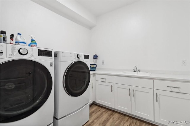 clothes washing area with washer and clothes dryer, sink, cabinets, and light wood-type flooring