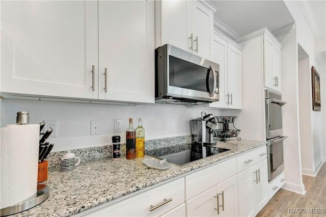 kitchen with white cabinetry, stainless steel appliances, light stone counters, and light wood-type flooring