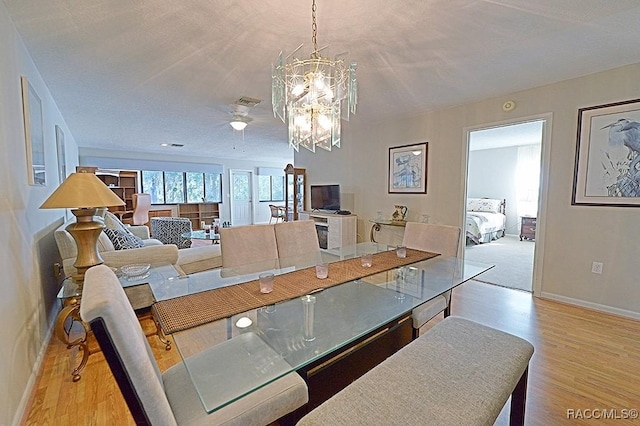 dining space with light hardwood / wood-style flooring, ceiling fan with notable chandelier, and a textured ceiling