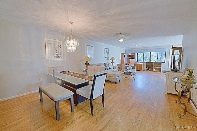 dining area with light hardwood / wood-style flooring, ceiling fan with notable chandelier, and a textured ceiling