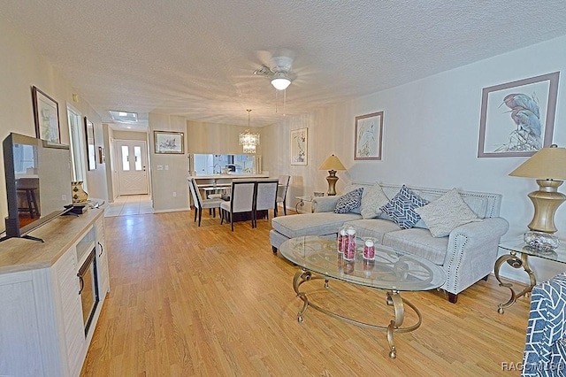 living room with ceiling fan with notable chandelier, a textured ceiling, and light wood-type flooring