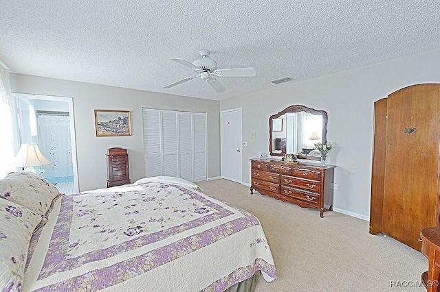 bedroom featuring light carpet, ensuite bath, a textured ceiling, ceiling fan, and a closet