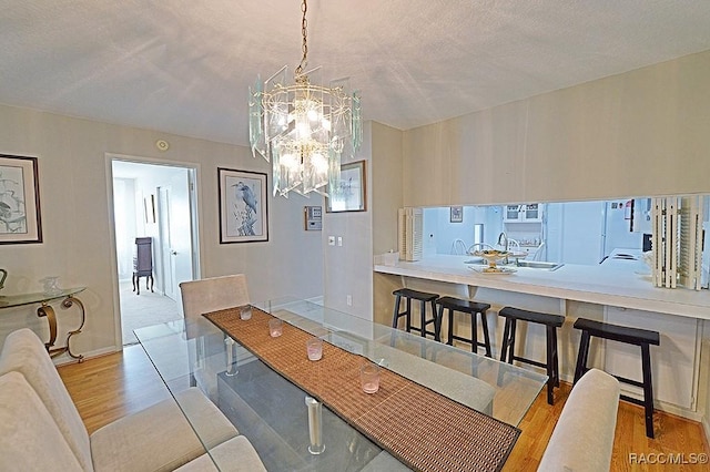 dining room with sink, light hardwood / wood-style floors, a textured ceiling, and an inviting chandelier