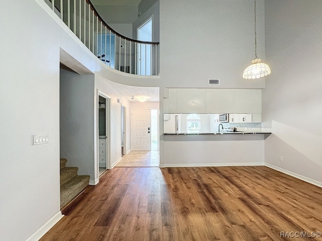 interior space with pendant lighting, white cabinets, dark hardwood / wood-style floors, a towering ceiling, and kitchen peninsula