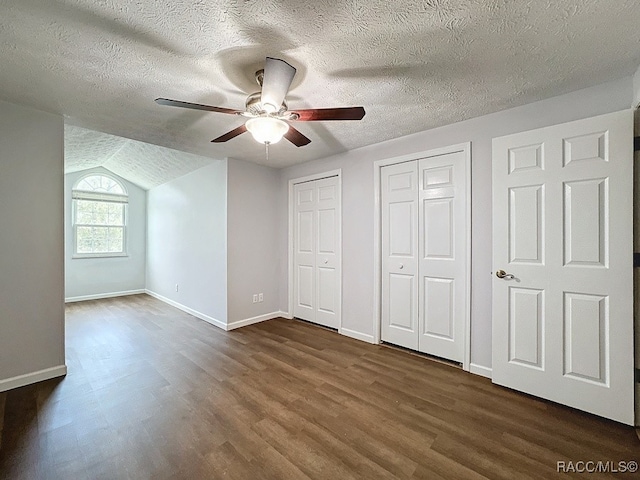 unfurnished bedroom featuring ceiling fan, dark wood-type flooring, a textured ceiling, vaulted ceiling, and two closets