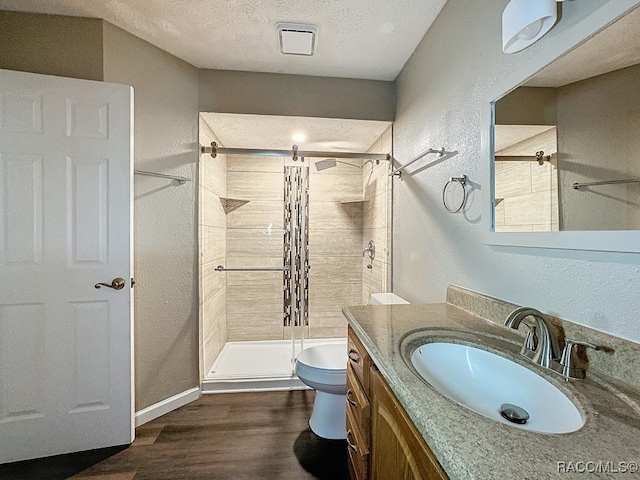 bathroom featuring wood-type flooring, a textured ceiling, toilet, tiled shower, and vanity