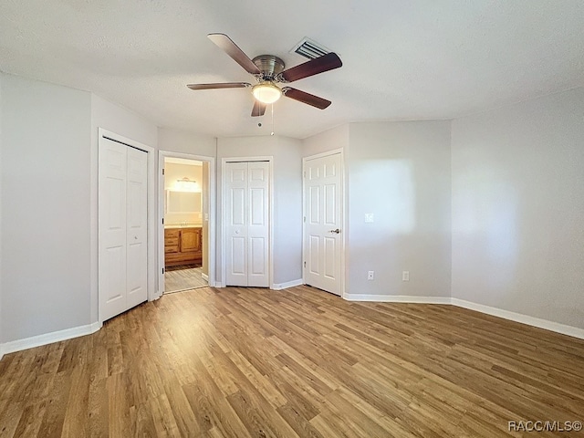 unfurnished bedroom with ceiling fan, ensuite bathroom, light wood-type flooring, and a textured ceiling