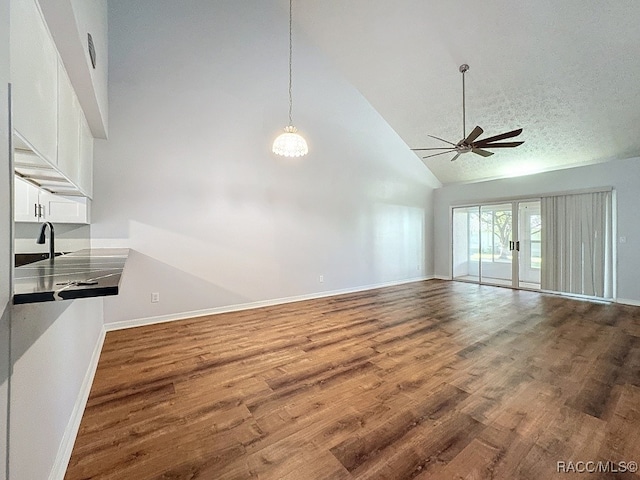 unfurnished living room featuring ceiling fan, high vaulted ceiling, a textured ceiling, and hardwood / wood-style flooring