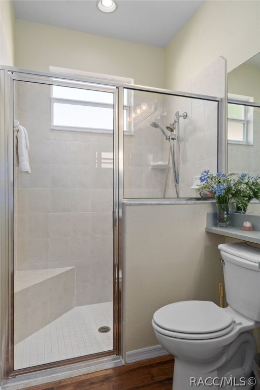 bathroom with wood-type flooring, a shower with door, toilet, and a wealth of natural light