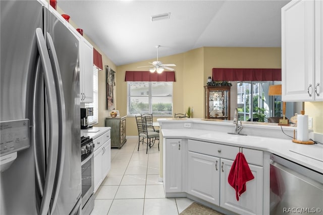 kitchen featuring lofted ceiling, sink, light tile patterned floors, appliances with stainless steel finishes, and white cabinetry