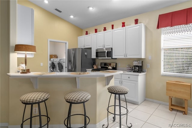 kitchen featuring stainless steel appliances, washing machine and dryer, lofted ceiling, a kitchen bar, and white cabinets