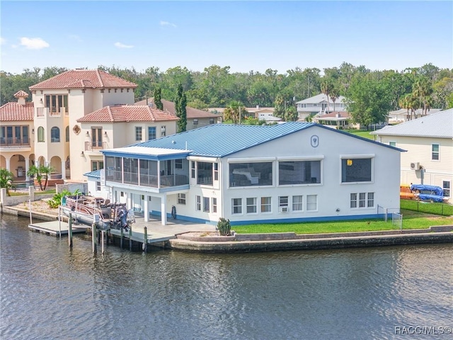 back of house featuring a residential view, stucco siding, a sunroom, and a water view