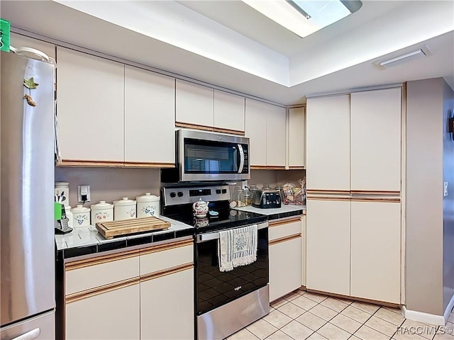 kitchen featuring white cabinetry, tile counters, appliances with stainless steel finishes, and light tile patterned floors