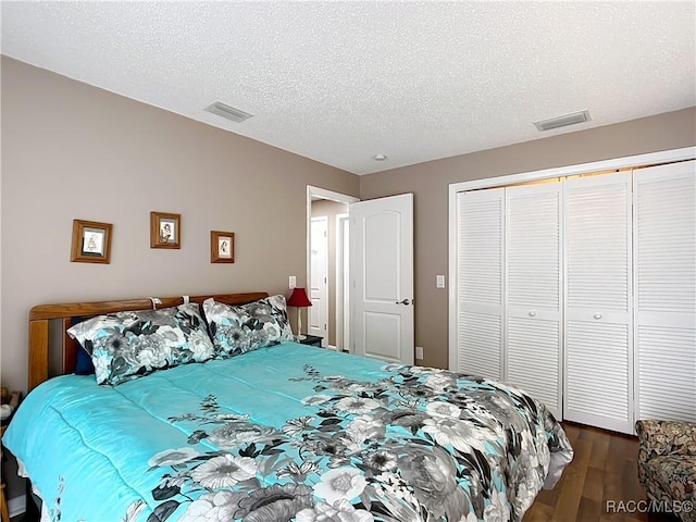 bedroom featuring a textured ceiling, a closet, dark wood-style flooring, and visible vents