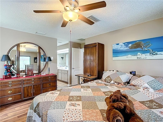 bedroom featuring light wood-style flooring, a textured ceiling, ensuite bath, and visible vents