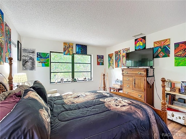 bedroom with visible vents, a textured ceiling, and wood finished floors