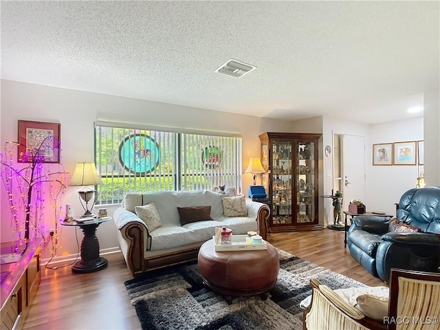 living room with visible vents, baseboards, wood finished floors, and a textured ceiling