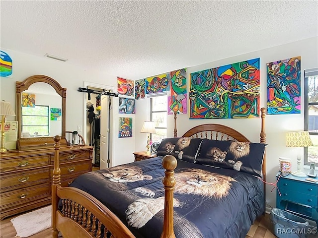bedroom featuring visible vents, a closet, a spacious closet, a textured ceiling, and wood finished floors