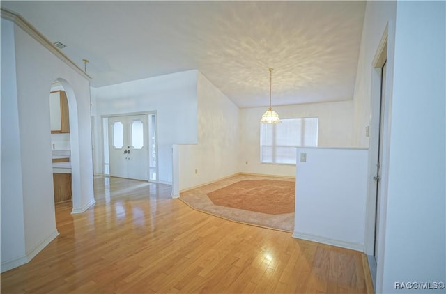 empty room featuring arched walkways, a chandelier, light wood-type flooring, and plenty of natural light