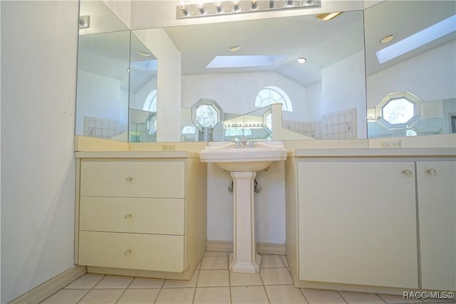 full bath featuring two sinks, vaulted ceiling with skylight, and tile patterned flooring