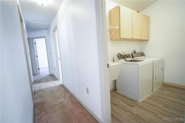 clothes washing area featuring washing machine and clothes dryer, light wood-style floors, cabinet space, and attic access