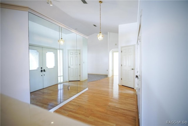foyer entrance featuring high vaulted ceiling, wood finished floors, arched walkways, and french doors