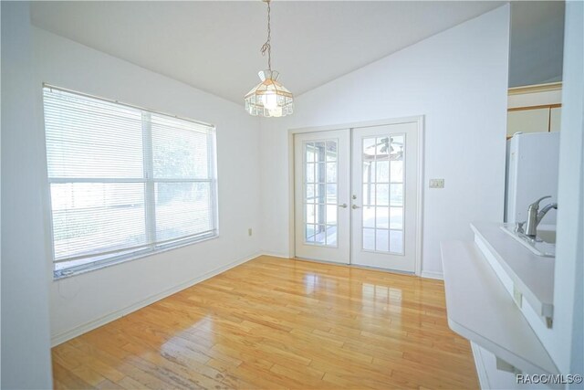 unfurnished dining area with a sink, lofted ceiling, light wood-style floors, and french doors