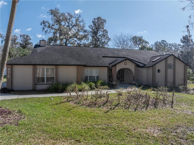 view of front of house featuring a shingled roof, a front yard, a chimney, and stucco siding