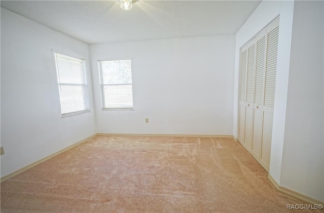 unfurnished bedroom featuring light carpet, baseboards, and a closet