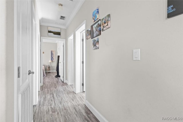 hallway with light wood finished floors, ornamental molding, visible vents, and baseboards