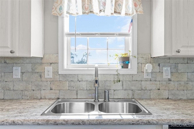 kitchen with tasteful backsplash, white cabinets, a sink, and light stone counters